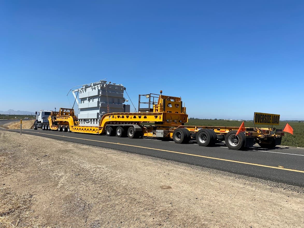 A Strategic Freight lowboy trailer hauling an oversize electrical transformer under an OVERSIZE LOAD banner